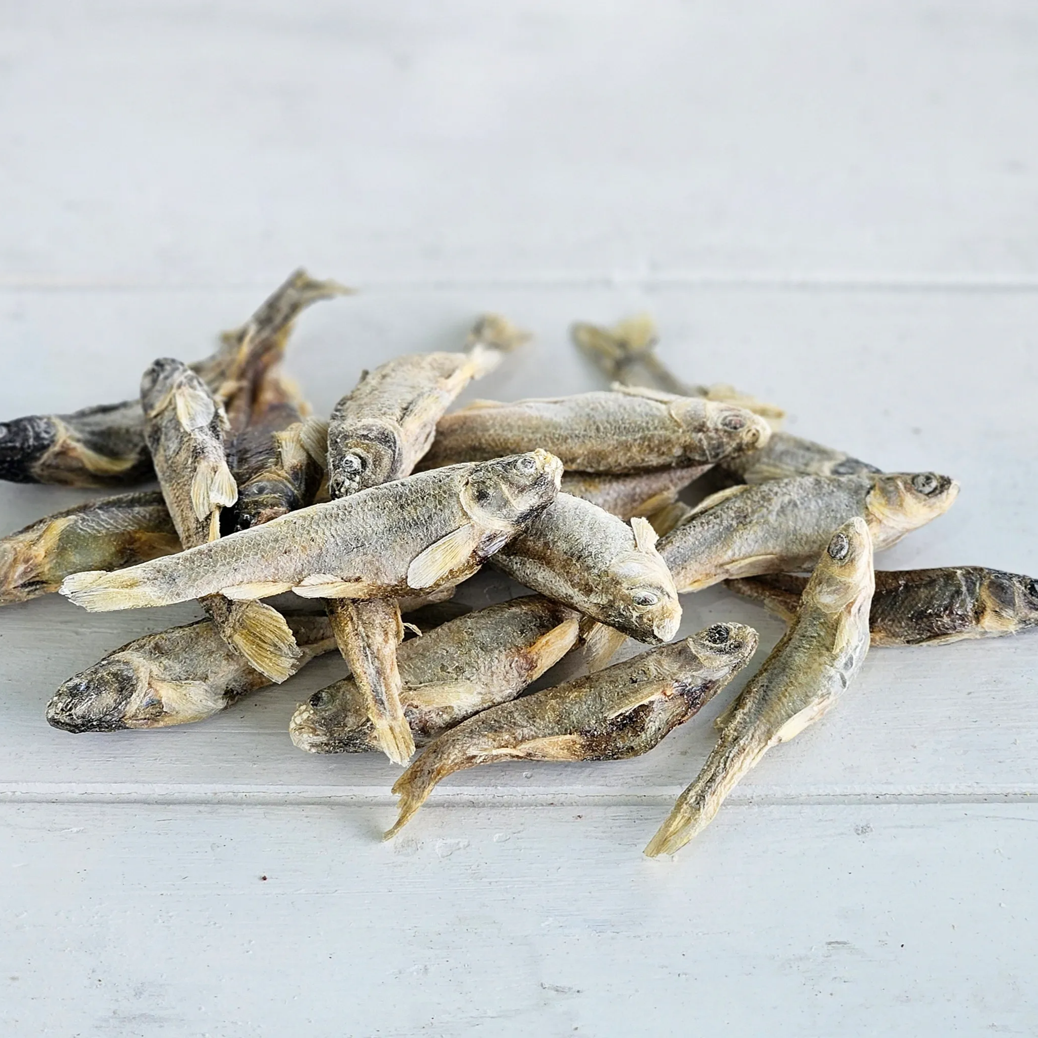 Whole freeze-dried minnows from Minnows Tasty Tidbits piled on a white wooden surface